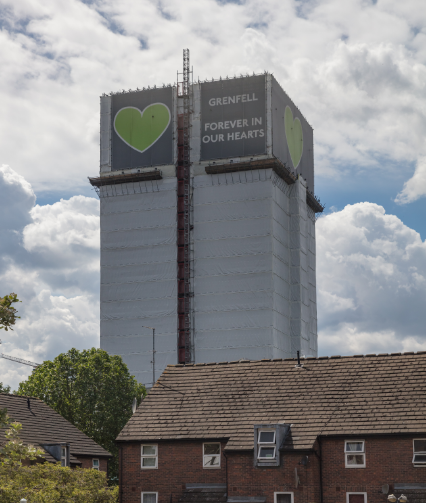 Grenfell Tower after fire, covered in scaffolding and green heart banner that reads: "Forever in our hearts"